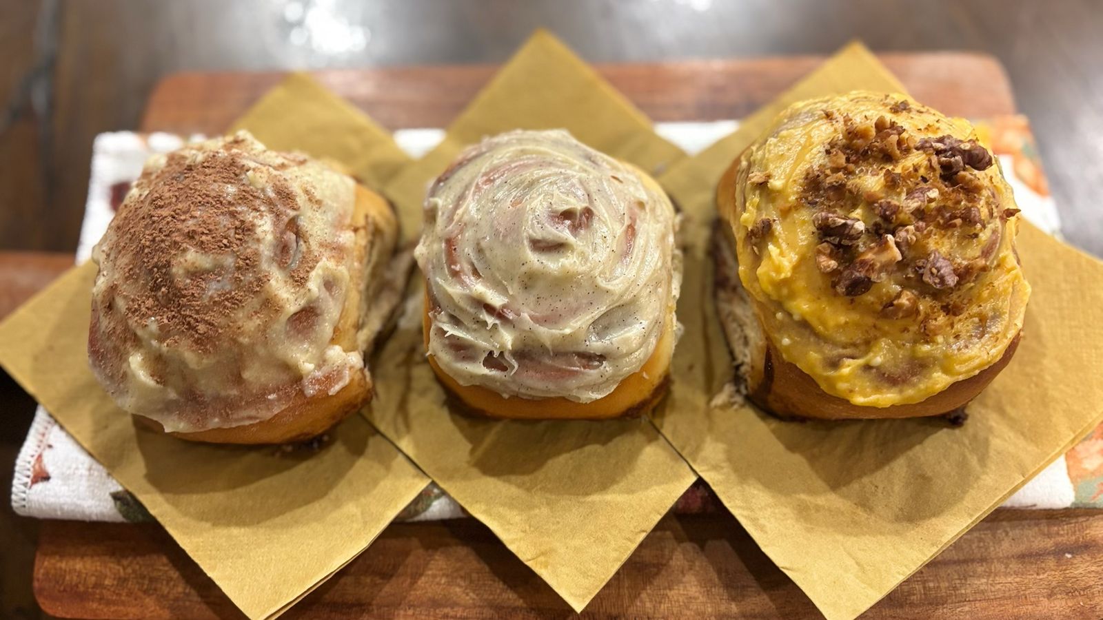 Three of Kylie's rolls on a wooden board: tiramisu, classic and pumpkin spice